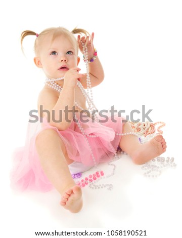 A beautiful 2-year-old with multiple strands of pink and white pearls.  She's wearing a shear pink tutu.  On a white background.
