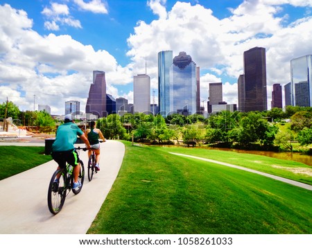 Riding Bikes on Paved Trail in Houston Park (view of river and skyline of downtown Houston) - Houston, Texas, USA  Royalty-Free Stock Photo #1058261033
