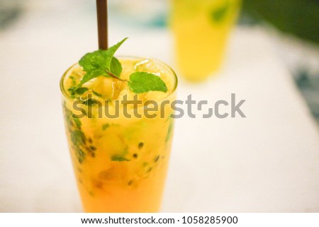 Close up and selective focus glass of ice passion fruit juice with soda on white wooden table in party night at restaurant or cafe.