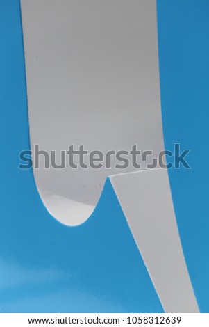Close up outdoor view of parts of big letters painted in clear blue and white. Modern abstract design. Shapes and curved forms in perspective, lighted by the sun. Bicolor image of sculpted objects.  