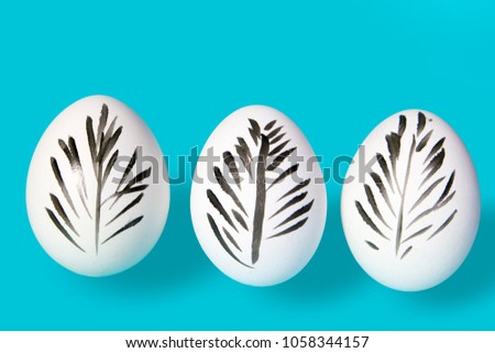 White hen eggs decorated for easter on a blue background. A black feather is drawn on the egg.
