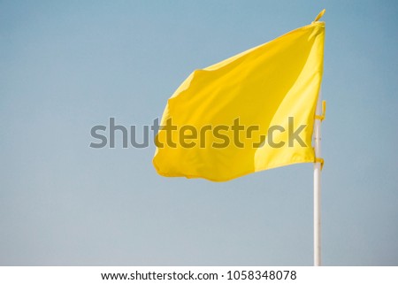 Bright yellow flag waves in the wind on a flagpole against a blue sky background close-up