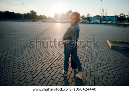 Beautiful young girl in sunglasses walk with skateboard at sunset