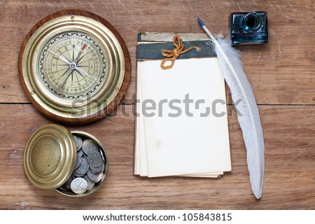 Compass, antique notebook, quill and inkwell, coins on wood