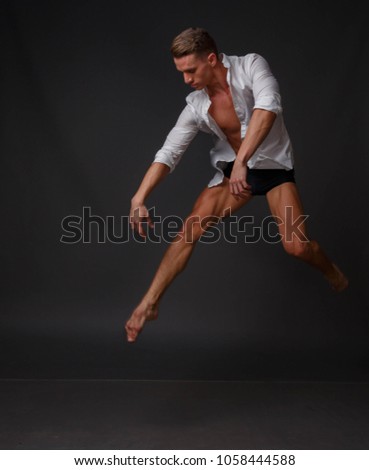 white man in an unbuttoned white shirt and black shorts dancing on a gray background, bare legs and torso, studio shot