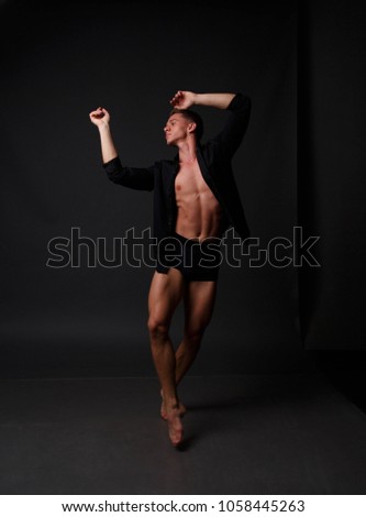 white man in an unbuttoned black shirt and black shorts dancing on a gray background, bare legs and torso, studio shot