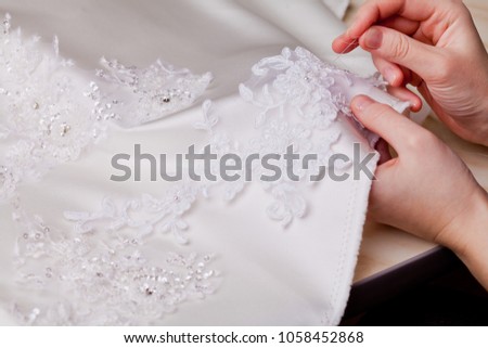 woman hands close up sewing a wedding dress, white material decorated with lace, tailoring clothes, white fabric