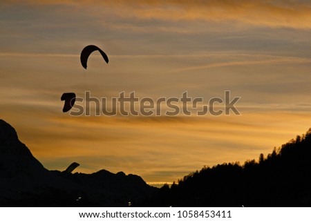 silhouettes of snowkiting at sunset