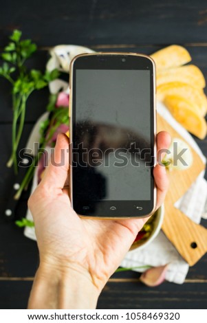Hand makes photo with phone of raw vegan dinner or lunch with avocado, nuts dip sauce and vegetables on wooden board. Empty screen. Smartphone food photography. Social networks. Vegetarian healthy