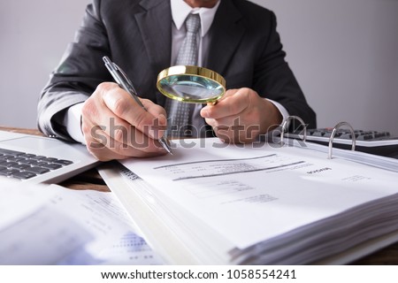 Close-up Of A Businessperson's Hand Looking At Receipts Through Magnifying Glass At Workplace Royalty-Free Stock Photo #1058554241