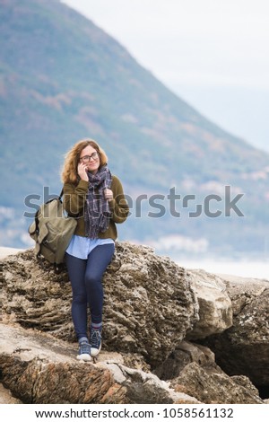 Woman traveler with phone standing on a rock on a sea coast 