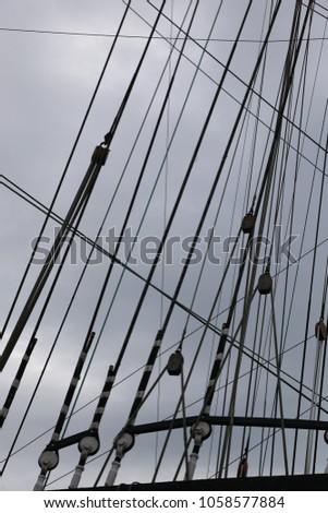 Close up outdoor view of the superior part of an ancient vessel. Silhouette of the mast and ropes in different directions. Cloudy grey sky in background. Pattern of crossing lines. Abstract image. 