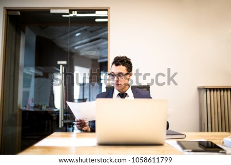Man proud CEO in glasses and formal suit monitors financial market via laptop computer, sitting in modern office interior. Male successful broker working on portable netbook. Economist using notebook 