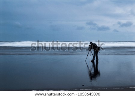 An abstract image of a photographer taking photos at dusk on a west coast beach in Auckland, New Zealand.