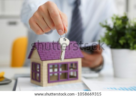 Male hand holds the key to the lock in the hand against the backdrop of the toy house sale purchase lease concept real estate services on the market.
