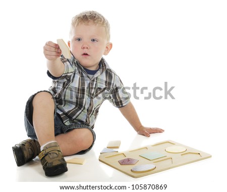 A young preschooler trying to figure out where the hexagon goes in his wooden shape puzzle.  On a white background.