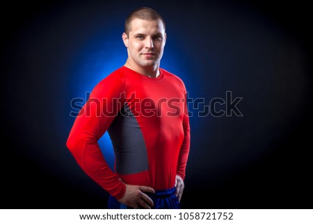 A strong dark-haired sportman  in a red sports wear  rush guard posing against a blue a lights on a black isolated  background 