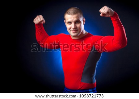 A strong dark-haired sportman  in a red sports wear  rush guard  show biceps against a blue a lights on a black isolated  background 