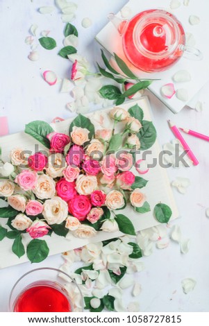 Spring reading concept with open book on a white background with flowers, rose petals, pink stationery and herbal tea. Feminine flat lay with copy space.