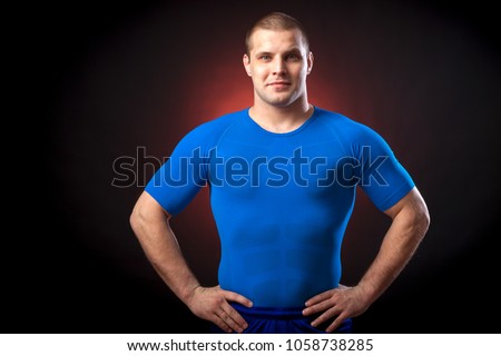 A strong dark-haired sportman  in a blue sports wear  rush guard posing against a red a lights on a black isolated  background 