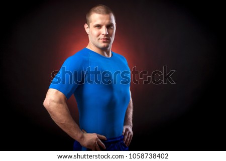 A strong dark-haired sportman  in a blue sports wear  rush guard posing against a red a lights on a black isolated  background 