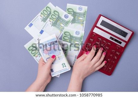 Female hands hold EURO bills and a calculator on a blue background - the concept of accounting
