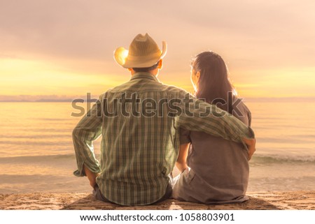 A cowboy with his lover are watching the sunset,Couple in love seated by the sea in the evening have sunset as the backdrop with rim light effect,A Men is embracing a women.