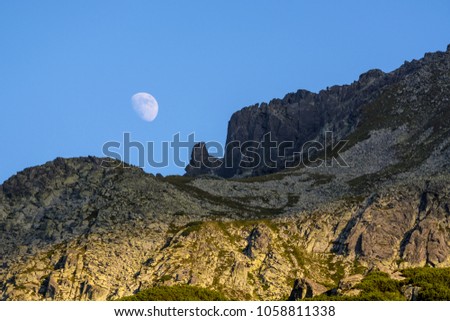Moonrise over the peak of a rocky mountains while the sun still illuminates the lower part of the picture