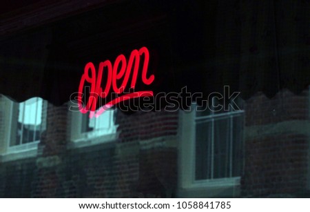 Red neon title on the shiny and blue light reflected window during the day. Ob background building with old fashion white framed windows. In foreground letters "open". Natural colors