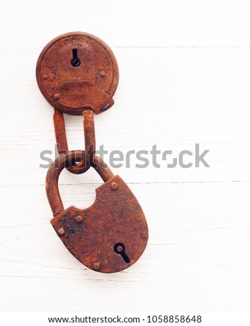 Two old rusty padlocks are fastened with each other on a white wooden background, close up