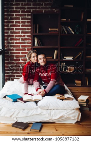 Beautiful smiling couple in red sweaters listening music, girlfriend leaning on handsome boyfriend, when he playing at gitar. Celebrating new year and xmas. Romantic winter holidays.
