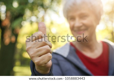 Smiling senior woman showing OK. Looking at camera. Focus is on hand.