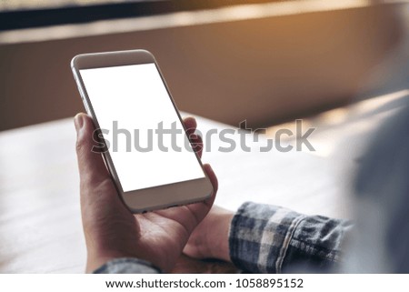 Mockup image of a hand holding white mobile phone with blank desktop screen in cafe