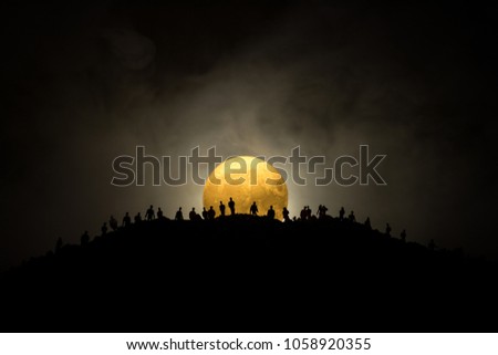 Scary view crowd of zombies on hill with spooky cloudy sky with fog and rising full moon. Silhouette group of zombie walking under full moon. Halloween concept.