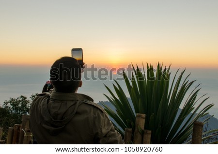 A Man is Holding Mobile Phone with his Hands to Take a Picture of Sunrise.