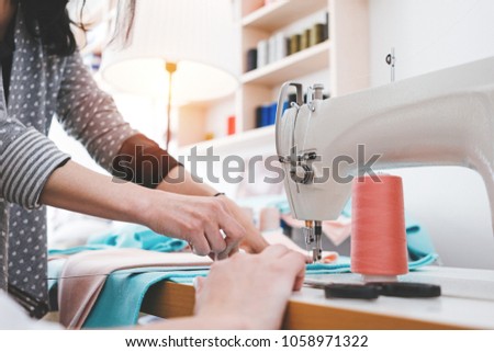 Young dressmaker woman working with cloth on sewing machine in design clothing bureau. Seamstress sew in workshop. Small business