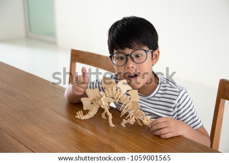 Happy Asian kid glad to finish making a 3D dinosour wood puzzle toy