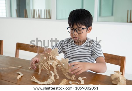 Happy Asian kid on the wood chair enjoy playing 3D dinosour wood toy
