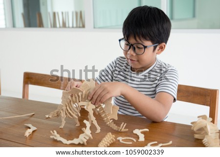 Happy Asian kid on the wood chair enjoy playing 3D dinosour wood toy
