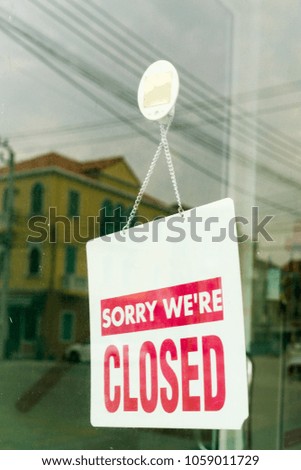 " Sorry we're closed " sign in red, hanging inside on shop glass door with city reflection.