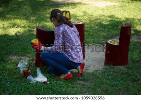 Summer work. Beautiful young girl paints a wooden garden table and chairs