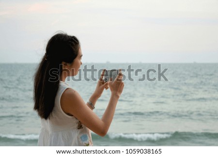Hands of the asian traveler girl taking a photo of the sea and sky by the smartphone at the beach.