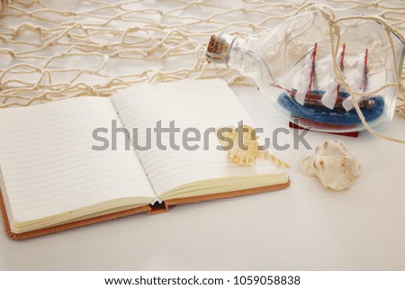 nautical concept image with sail boat in the bottle and empty open notebook over white wooden table