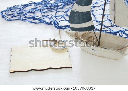 nautical concept image with white decorative sail boat and empty wooden board over white table