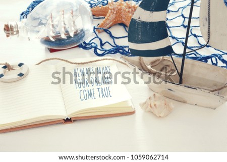nautical concept image with white decorative sail boat and notebook: ALWAYS MAKE YOUR DREAMS COME TRUE