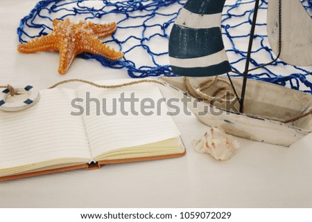 nautical concept image with white decorative sail boat and empty open notebook over white wooden table
