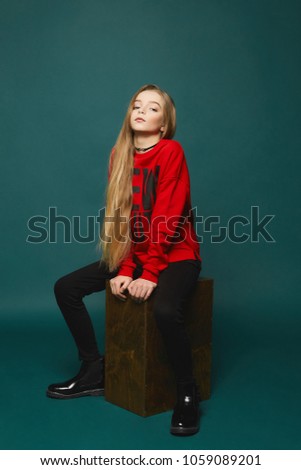 Stylish teen girl with long blonde hair posing in studio at dark-green background