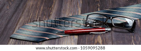 Men's accessories to work on brown wooden background. Tie, glasses, fountain pen. Horizontal photo