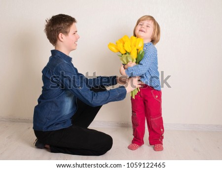 Little girl with flowers kissing her elder brother. Teen boy congratulates his little sister and gives her flowers tulips.