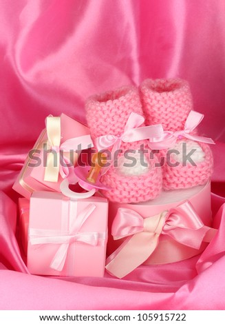 pink baby boots, pacifier, gifts on silk background